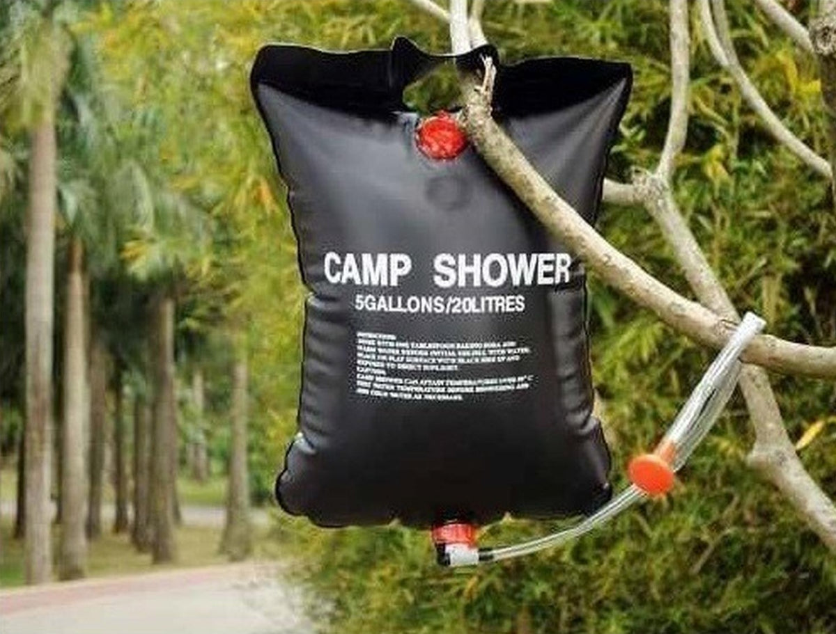 Ducha Solar Camping 20 L Lhotse colgada de una rama en el bosque, con su manguera y regadera